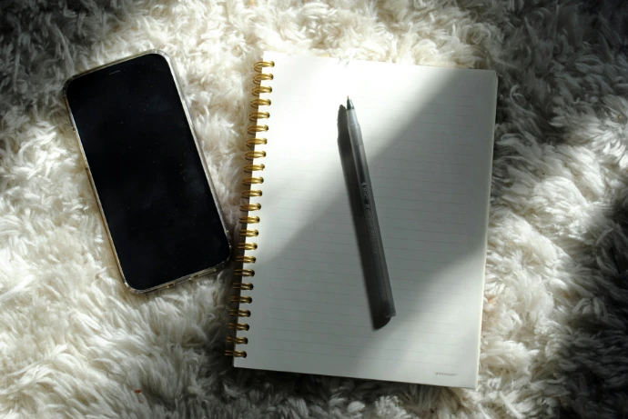 a notepad, pen, and phone on a fluffy surface